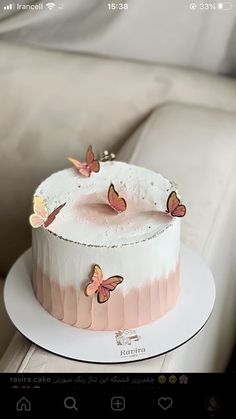 a white cake with pink icing and butterflies on it sitting on a plate next to a couch