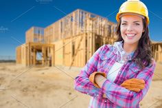 a woman wearing a hard hat and gloves in front of a construction site with her arms crossed