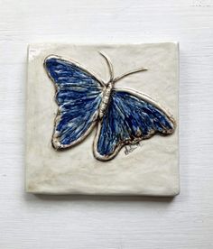 a blue butterfly on a white tile with silver trimmings and an intricate design