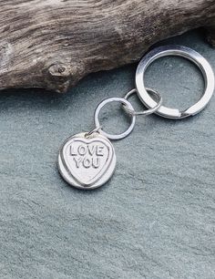 a keychain with the words love you on it sitting next to a piece of driftwood