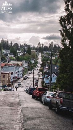 cars are parked on the street in front of houses and trees, with dark clouds overhead