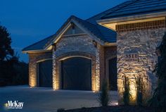 a house with lights on the side of it and a garage door in front of it