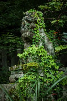 a stone statue covered in green plants next to trees