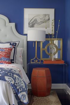 a bedroom with blue walls and an orange ottoman in the corner, along with a white headboard