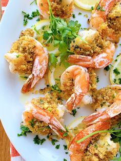 a white plate topped with shrimp next to lemon wedges and garnished with parsley