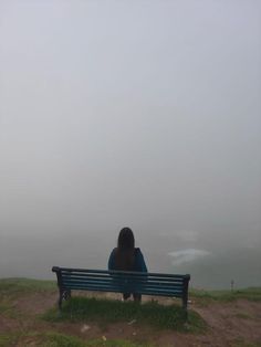 a woman sitting on top of a blue bench in the middle of a foggy field