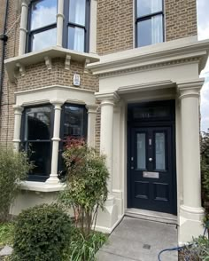 a black door is in front of a brown brick building with two windows and bushes