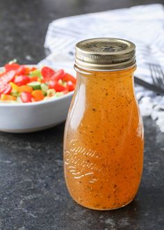 a glass jar filled with dressing next to a bowl of salad on a counter top