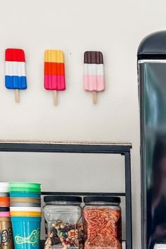 three popsicles are hanging on the wall next to some cups