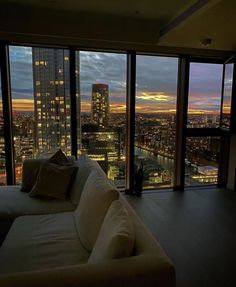 a living room filled with furniture and large windows overlooking the city at sunset or dawn