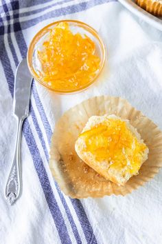 a bowl of orange marmalade sits next to a muffin on a paper plate