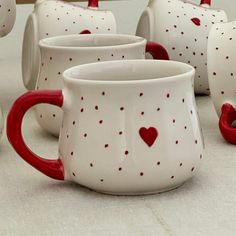 red and white coffee mugs with hearts painted on them sitting on a tablecloth