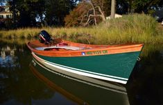 a green and white boat sitting on top of a body of water next to tall grass