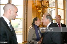 two men and one woman are talking to each other in front of a chandelier