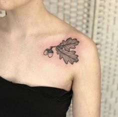 a woman wearing a black dress has a tattoo on her shoulder and is holding an acorn