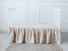 a white crib with a beige bed skirt on the bottom, and a round rug underneath it