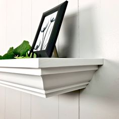 a white shelf with a black frame and some flowers on the ledge next to it