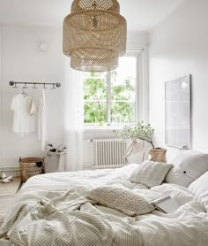 a bed sitting in a bedroom next to a white dresser and window with a wicker basket hanging from the ceiling