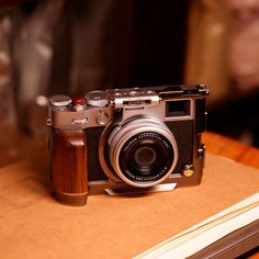 an old fashioned camera sitting on top of a wooden table next to a book and pen