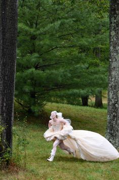 a woman dressed in white is walking through the woods with her dress flowing down to her chest