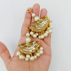 a hand holding two gold and white earrings