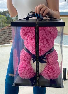 a woman holding a large pink teddy bear in a clear box with black ribbon around its neck