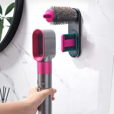 a person holding a hair dryer and brush in their hand next to a wall