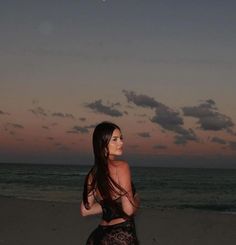 a woman standing on top of a sandy beach next to the ocean at night time