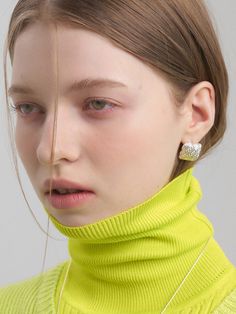 a woman wearing yellow sweater and silver earring on top of her head, looking off to the side