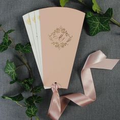 a pink wedding card with a monogrammed initial on it next to greenery