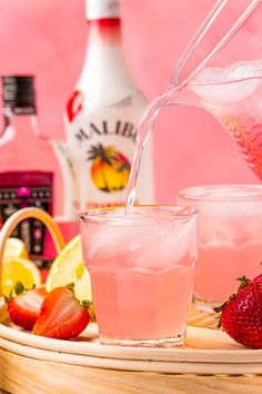 a pitcher pouring water into a glass with strawberries and lemons on the side