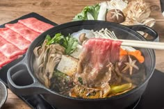 a pot filled with meat and veggies on top of a wooden table next to chopsticks