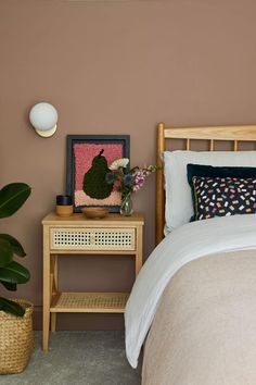 a bed room with a neatly made bed next to a night stand and potted plant