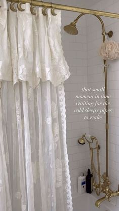 the shower curtain is white and has gold hardware on it, along with an antique brass faucet