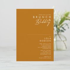 an orange and white bridal tea party card on a marble table with flowers in the background