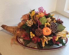 an arrangement of autumn flowers and leaves on a platter with a window in the background