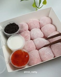 a box filled with pink donuts next to some dipping sauces and a green plant