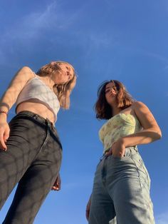 two young women standing next to each other in front of a blue sky with clouds