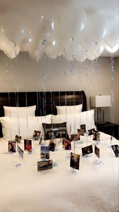 balloons are floating from the ceiling above a bed with white sheets and pillows on it