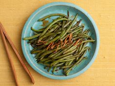 a blue bowl filled with green beans next to chopsticks