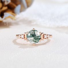 an oval cut green and white stone ring with three diamonds around it on a white surface