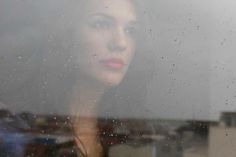 a woman standing in front of a window covered in rain