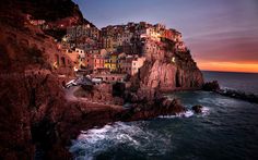 a small village on top of a cliff next to the ocean at sunset or dawn