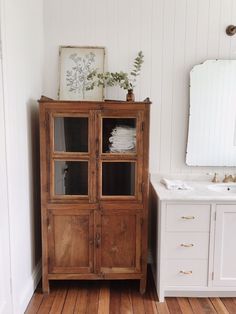 a wooden cabinet sitting next to a white sink in a room with wood floors and walls