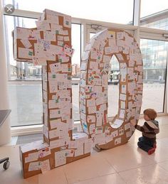 a little boy sitting on the floor next to a large letter made out of cardboard