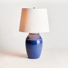 a blue table lamp with a white shade on the base and a light in front of it