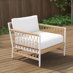 a wicker lounge chair with white cushions on a wooden deck in front of a fence