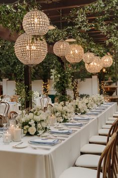 a long table is set with white flowers and greenery for an outdoor wedding reception