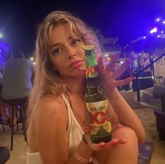 a woman sitting at a table with a beer bottle in her hand while holding it up