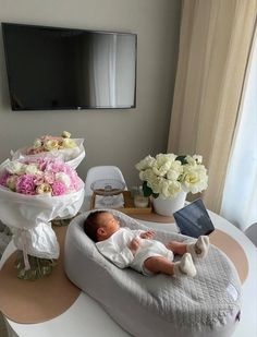 a baby laying on top of a bed next to a table with flowers and a laptop